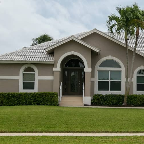 A grey-tan home in a tropical climate with a palm tree, suggesting a serene living environment.