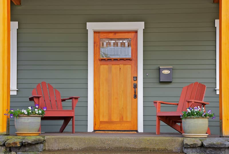 Front door and entryway of a home with an orange door and red colored wooden chairs on the porch.