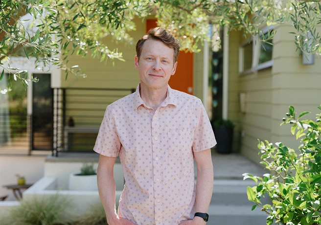 Man standing outside a home in a pink shirt.