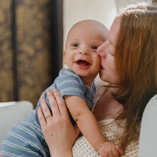 Mother kissing baby on cheek at home on couch.