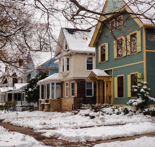 A quiet residential street lined with homes with snow on the ground.