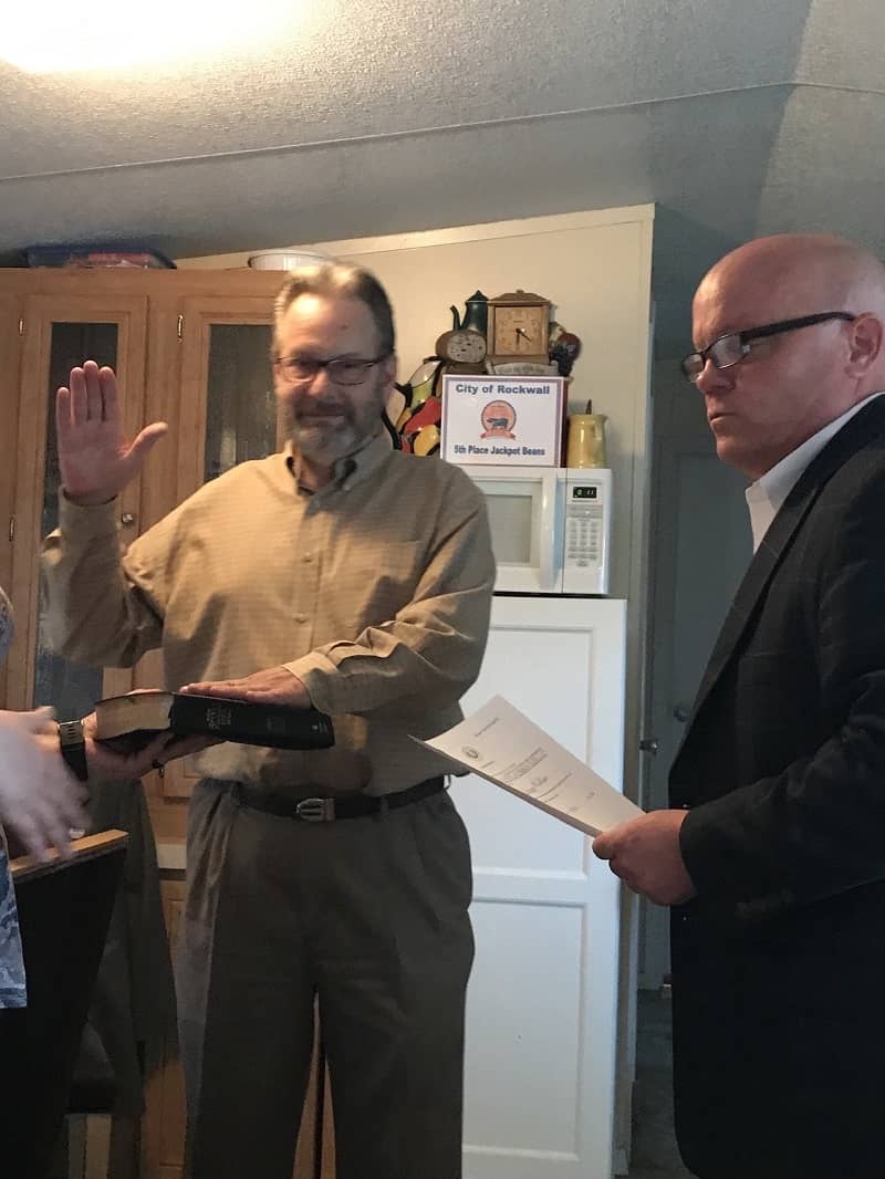 Man holding one hand up and one hand of Bible being sworn into office.