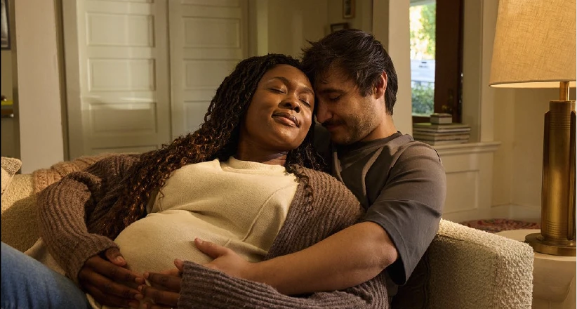 A couple sitting on a couch, with the pregnant woman resting and the man holding her belly supportively.