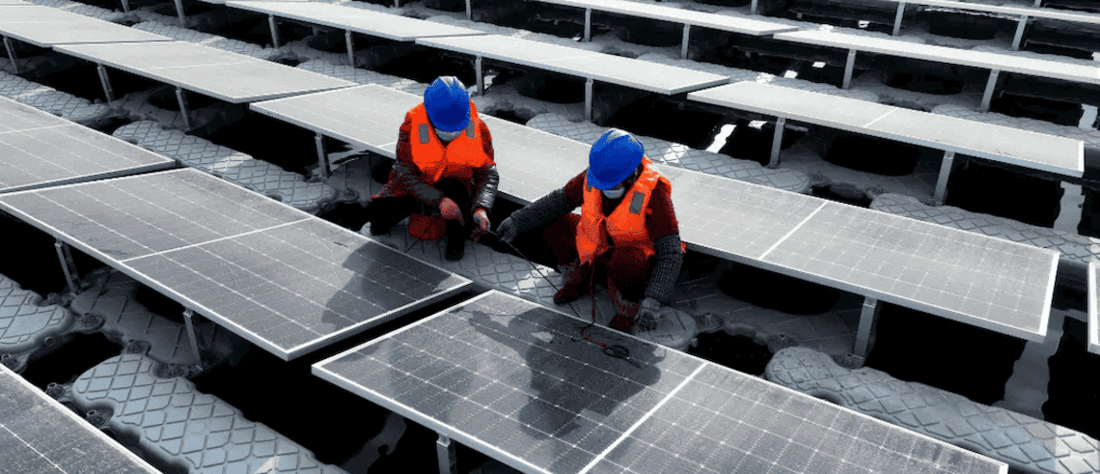 Solar technicians in hard hats working on solar panel farm.