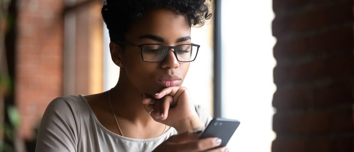 A young woman looking at her cell phone with a neutral expression.