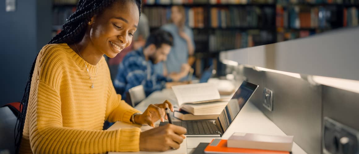 A black woman writing notes in a library or study setting.