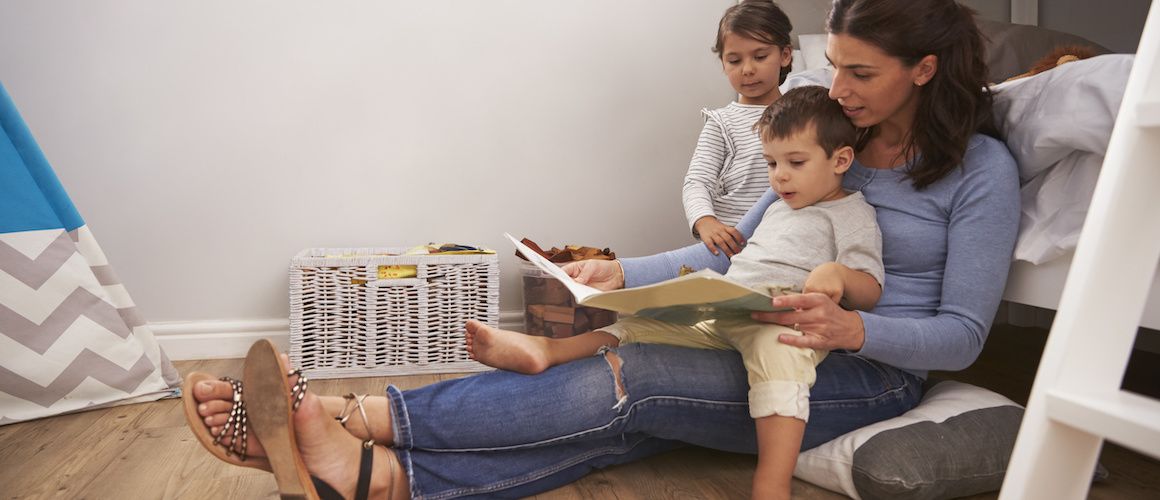 Image of mom sitting on floor, reading to children.