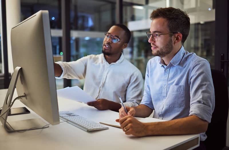 Two men in business attire looking at a large computer monitor together.