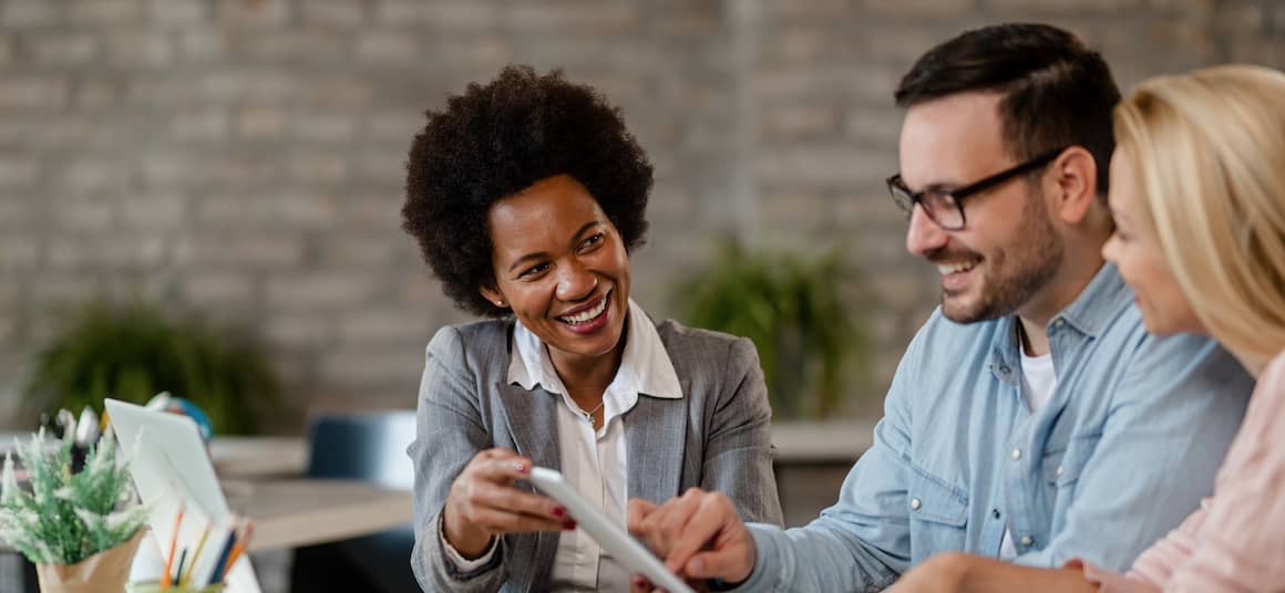 Real estate agent pointing to listings on tablet as he discusses options with hopeful couple seeking to purchase a home.