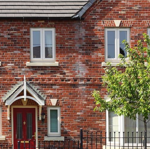 Exterior view of an English-style red brick house with a garden and driveway.
