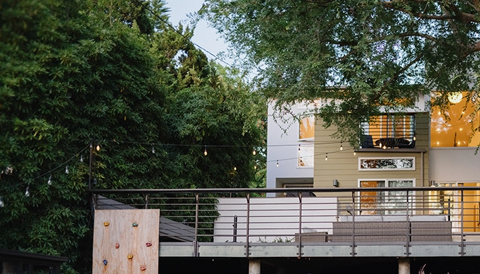 House surrounded by trees on a large hill wiht a climbing wall and concrete steps.