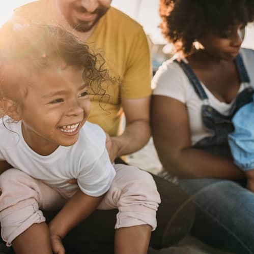 Family with young kids snuggling on sunny beach together.