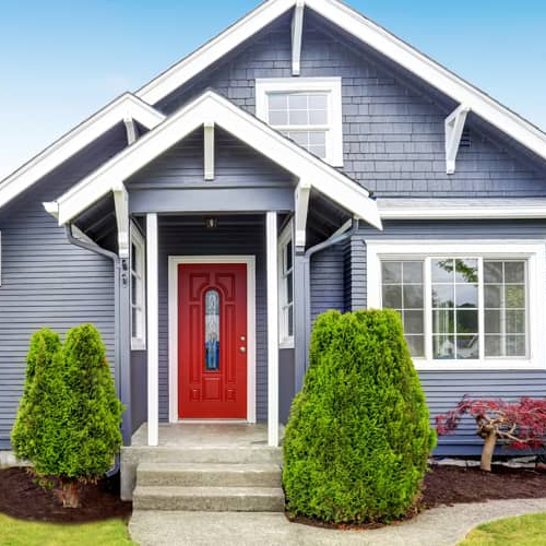 A small indigo colored house with a red door and green front yard.