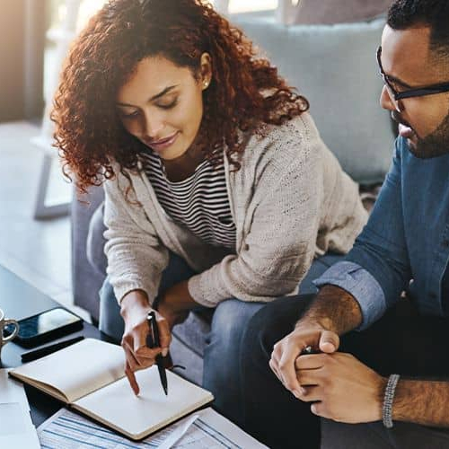 A man and woman sitting on a couch, possibly researching or reviewing real estate information in a book.
