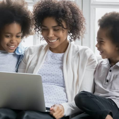 A Black woman with her daughters on a couch, looking at a computer, potentially in a home setting.