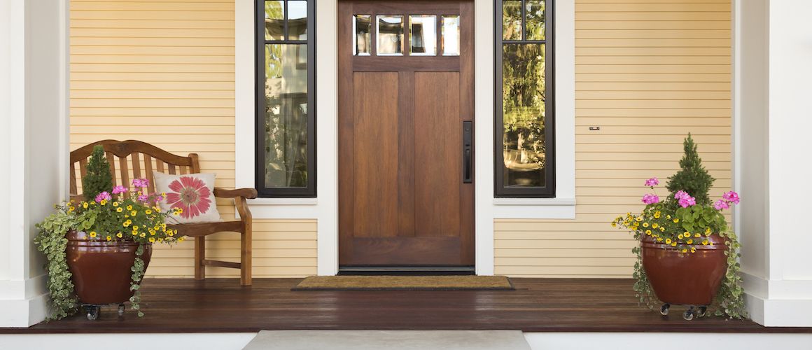 Front porch of a home with a brown front door framed by small rectangular windows.