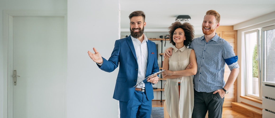 A real estate agent with a clipboard in hand showing house to a couple.