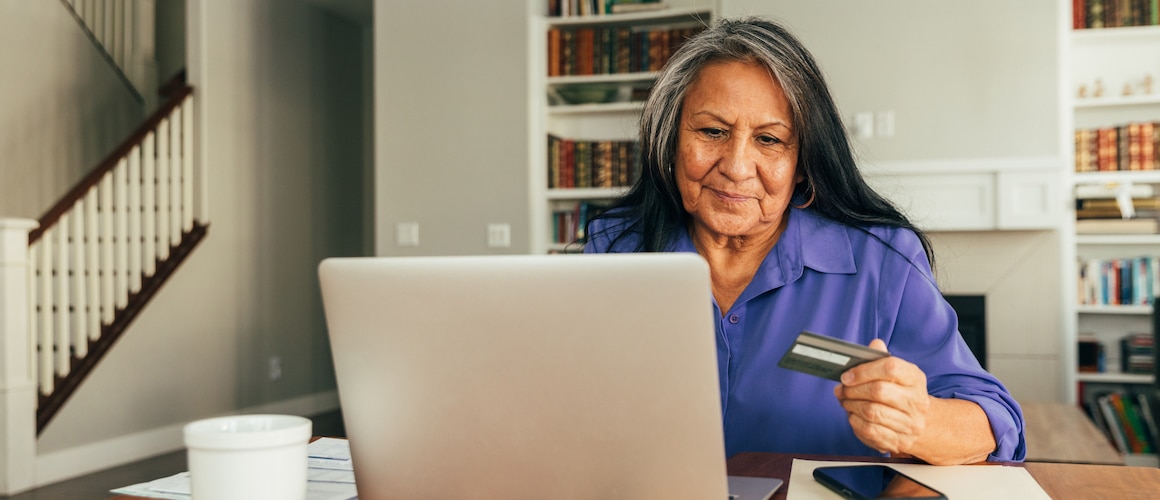 Indigenous woman looking at her laptop while holding a credit card.