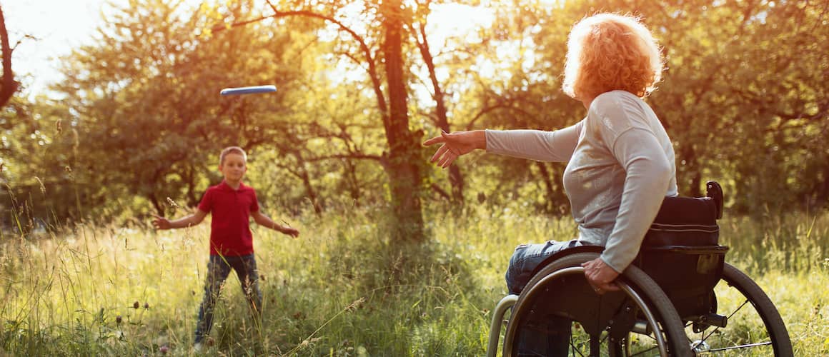 A mother in a wheelchair playing frisbee, depicting a mother in a wheelchair enjoying outdoor activities.