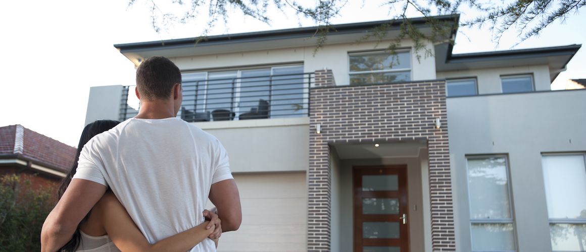 A couple standing in front of a house, possibly homeowners.