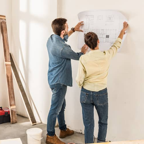 A couple examining blueprints against a wall, potentially involved in home renovation or construction planning.