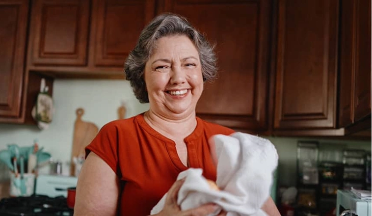 A woman standing in her kitchen holding a towel.