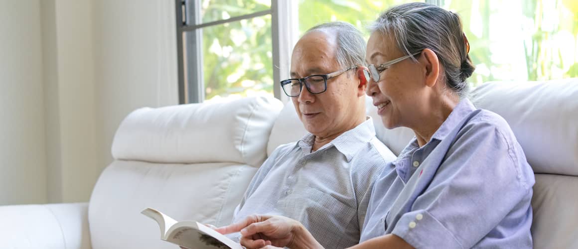 An older couple on a couch with a book, depicting relaxation or leisure time at home.