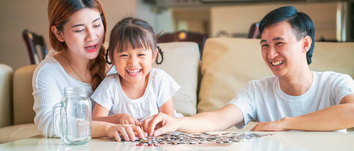 Parents with their young child counting coins with an empty mason jar nearby.