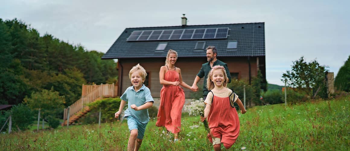 A happy family running near a house with solar panels, indicating an eco-friendly or sustainable home setting.