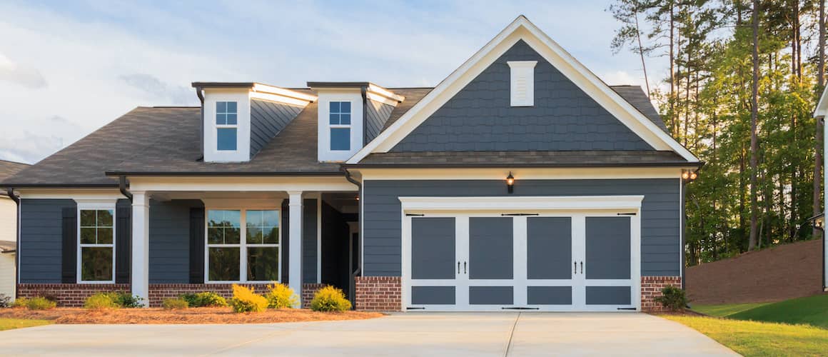 An image displaying a grey, single-story ranch-style model house with a well-maintained lawn and driveway.