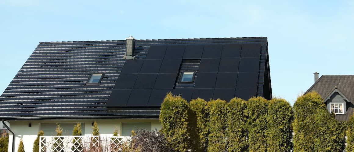 Black roof of house with black solar panels against backdrop of blue sky.