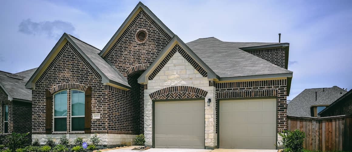 A dark brown and light brown speckled brick home with a white sandstone garage, showcasing unique exterior materials.