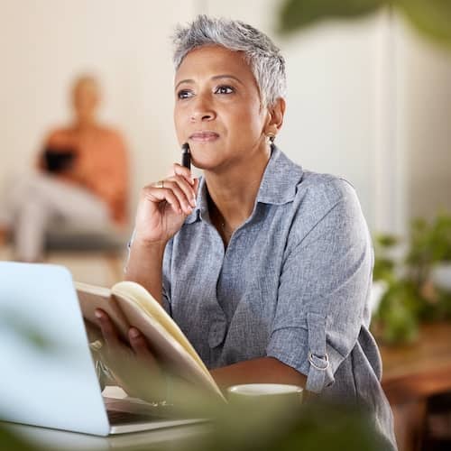 A woman in deep thought with a notebook in hand and resting her chin against a pen.