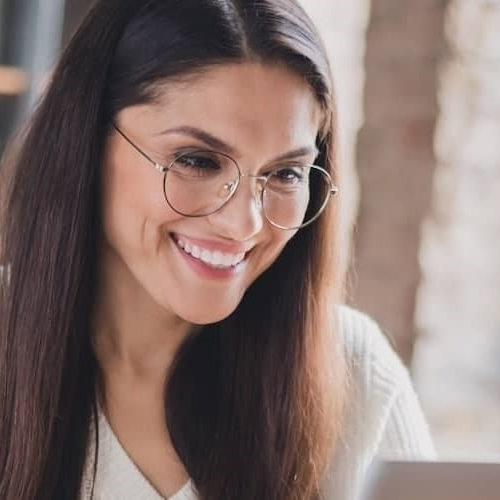 A lady with glasses looking extremely happy while using her laptop.