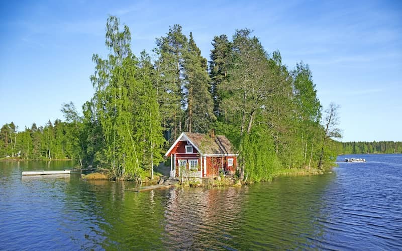 Small, summer cottage set on a point with calm, blue water and wooden dock in front and lined with forest in the back. 