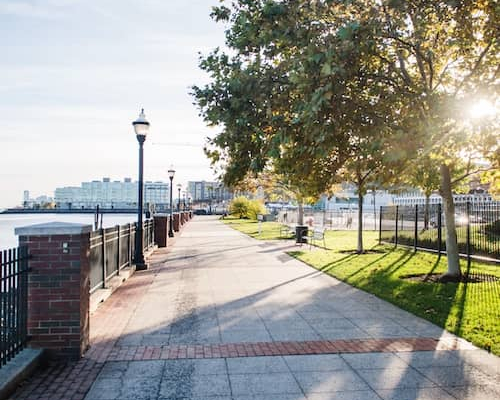 Tree lined walkway along waterfront with skyline in distance in West New York, New Jersey.