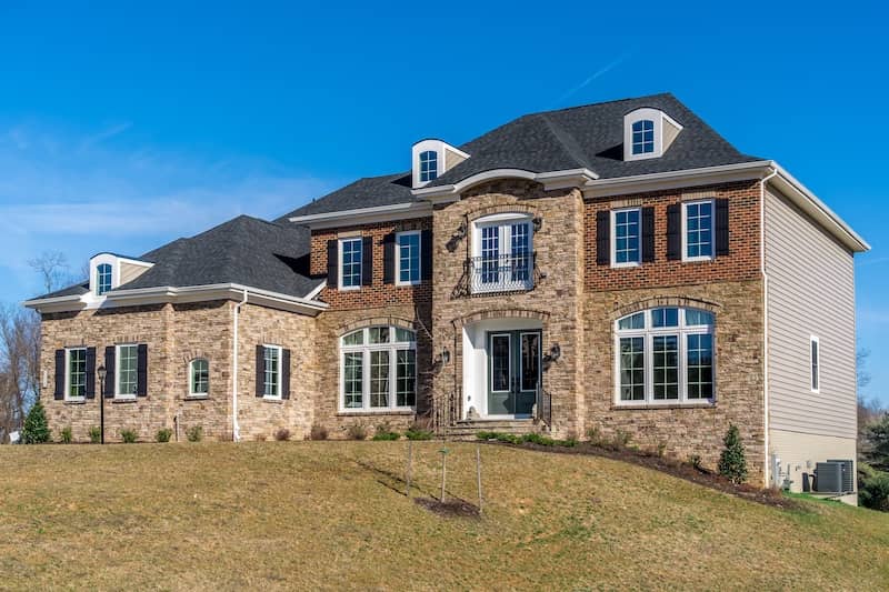 Red brick mcmansion on side of hill with beige siding.