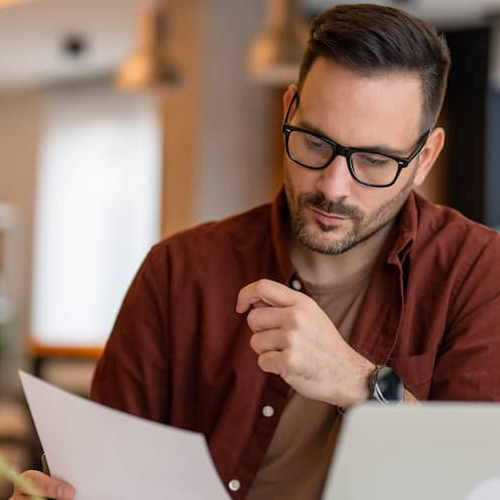 A man using a computer in a room filled with plants, perhaps indicating a home office or a relaxed workspace.