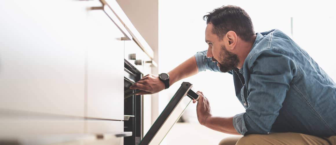 man squatting and looking inside oven