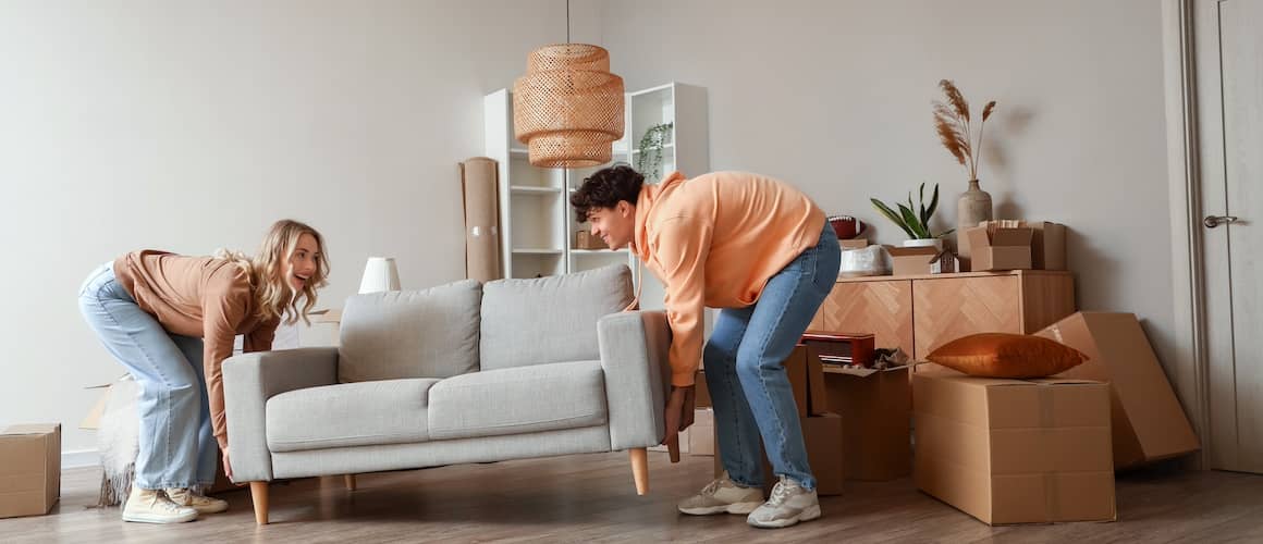 Young couple carrying a couch into a new home filled with cardboard boxes.