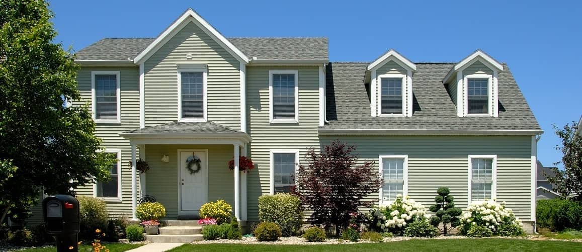 A green two-story house by a tree.