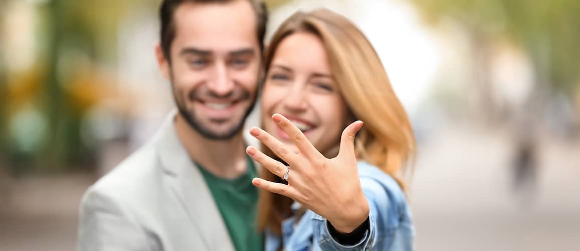 Happy engaged couple showing engagement ring on woman in selfie.