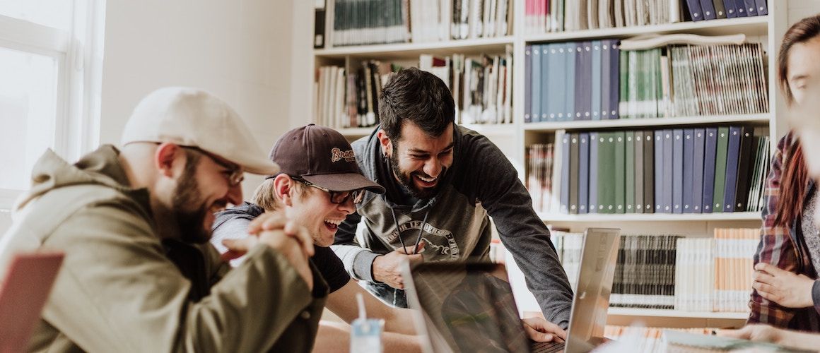 Image of happy students in library looking at finances on computers.