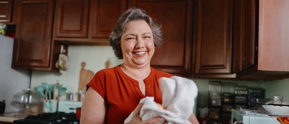 Woman in kitchen, drying dishes and smiling.