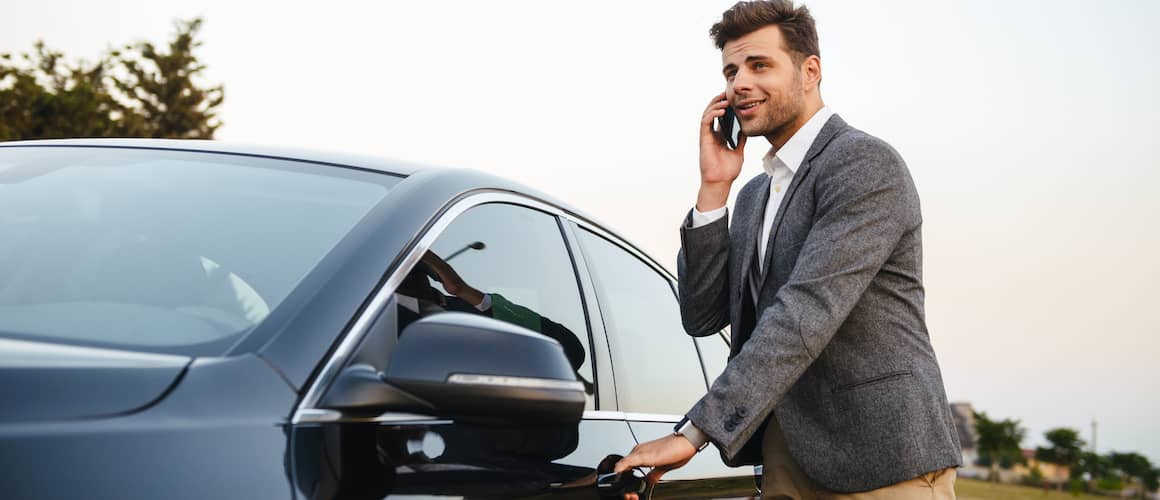 Man in business attire speaking on phone while entering his car.