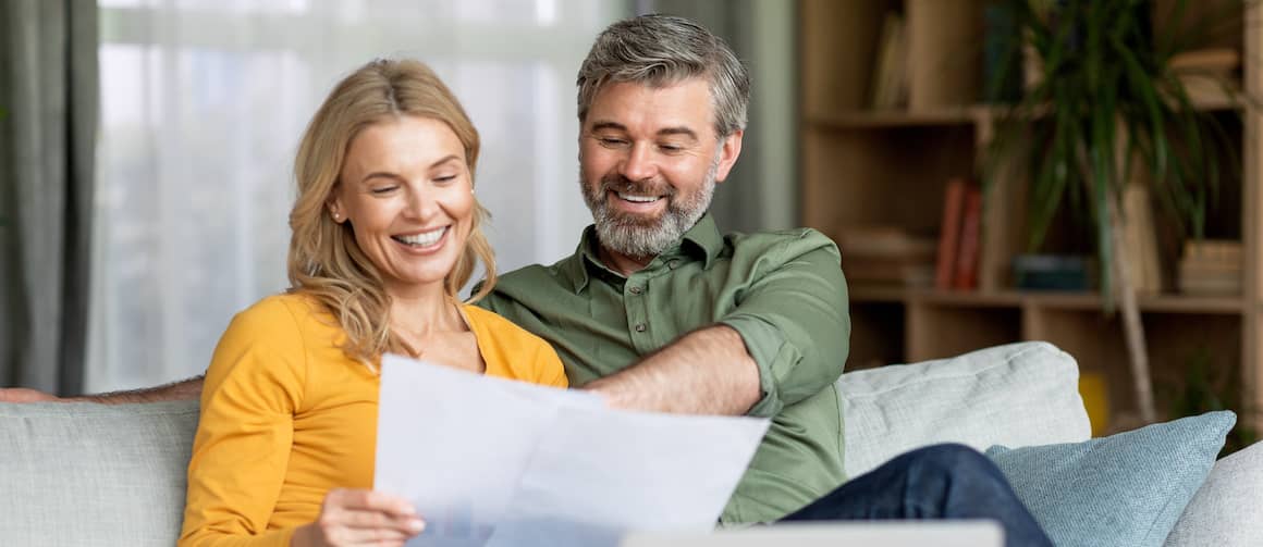 Middle-aged couple looking at paperwork together and smiling.