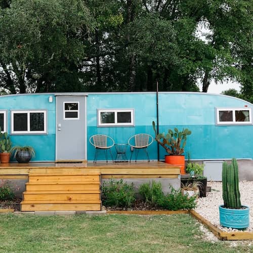Blue vintage mobile home with built on deck and large potted plants.