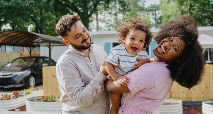Couple holding a smiling child outdoors in front of their home