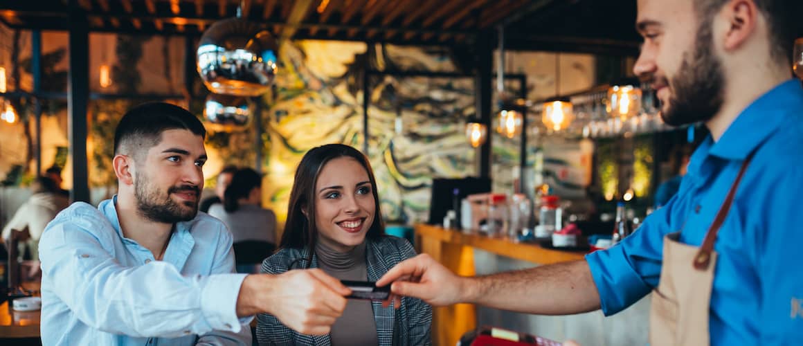 Young couple sitting at a restaurant as the man hands his card to the server to pay.