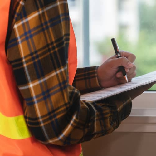 Home inspector standing in front of a window, possibly inspecting a property with a clipboard in hand.
